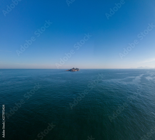 Solitary island in the middle of a vast blue sky and ocean at sunrise
