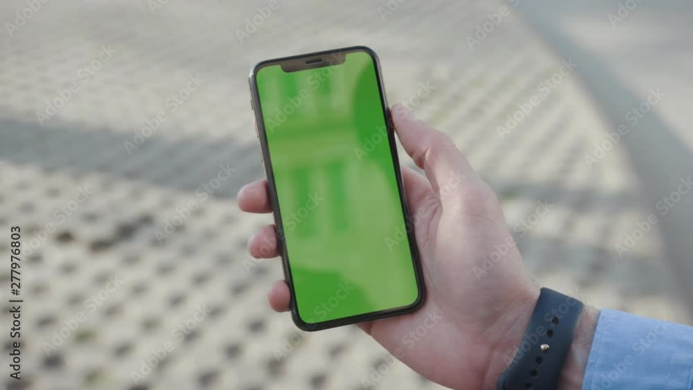 NEW YORK - April 5, 2018: Sunlight hands young man holding a smartphone with vertical green screen background city touchscreen wireless business evening cellphone communication device digital internet NEW YORK - April 5, 2018: Sunlight hands young man holding a smartphone with vertical green screen background city touchscreen wireless business evening cellphone communication device digital internet