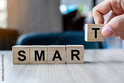 Businessman hand holding wooden cube block with SMART business word on table background. Specific, Achievable, Measurable, Realistic and Timely concepts photo