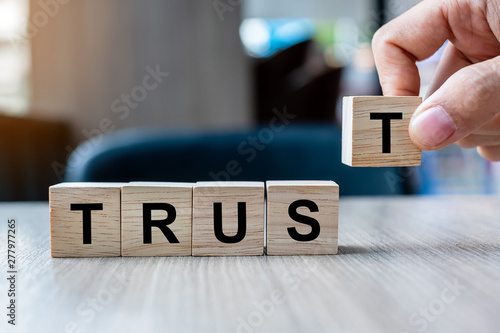 Businessman hand holding wooden cube block with TRUST business word on table background. Trustworthy, Truth, beliefs and agreement concept