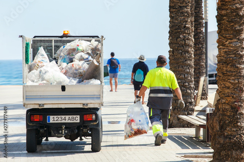Worker cleaning trash on street of seaside. Cleaning service with worker and car, Spain, Europe.