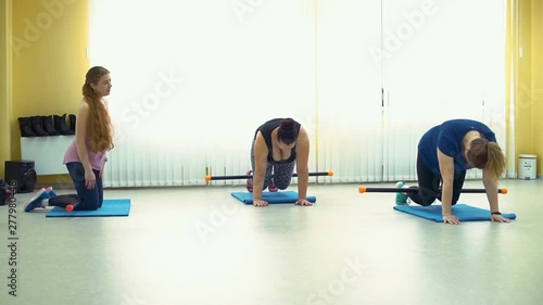 Overweight Women Exercising under the Supervision of the Personal Trainer in a Gym. They Doing Physical Training on mats with Barbells. photo