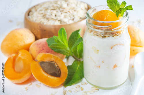 Oatmeal milkshake, smoothie or yogurt with fresh apricot on a white wooden table.
