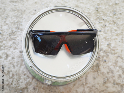Closeup of dirty safety glasses on a can with white paint.