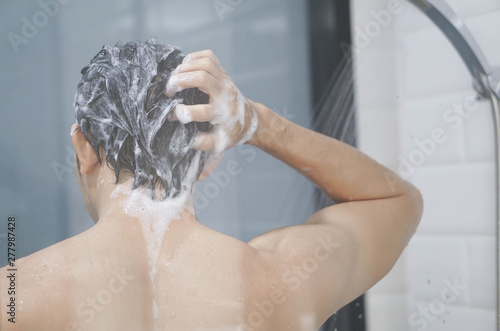 Closeup young man washing hair with with shampoo in the bathroom, vintage tone, selective focus