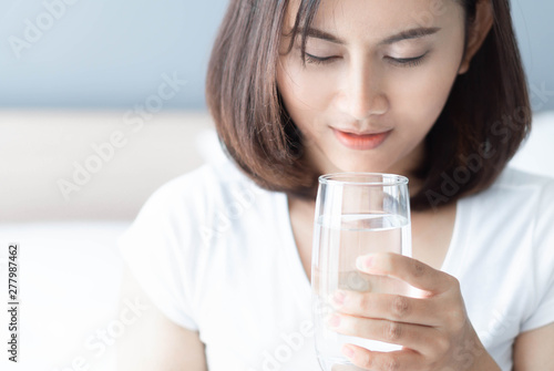 Close up woman drinking pure water from glass with light in the morning, Selective focus