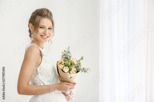 Beautiful young bride with bouquet of flowers near window