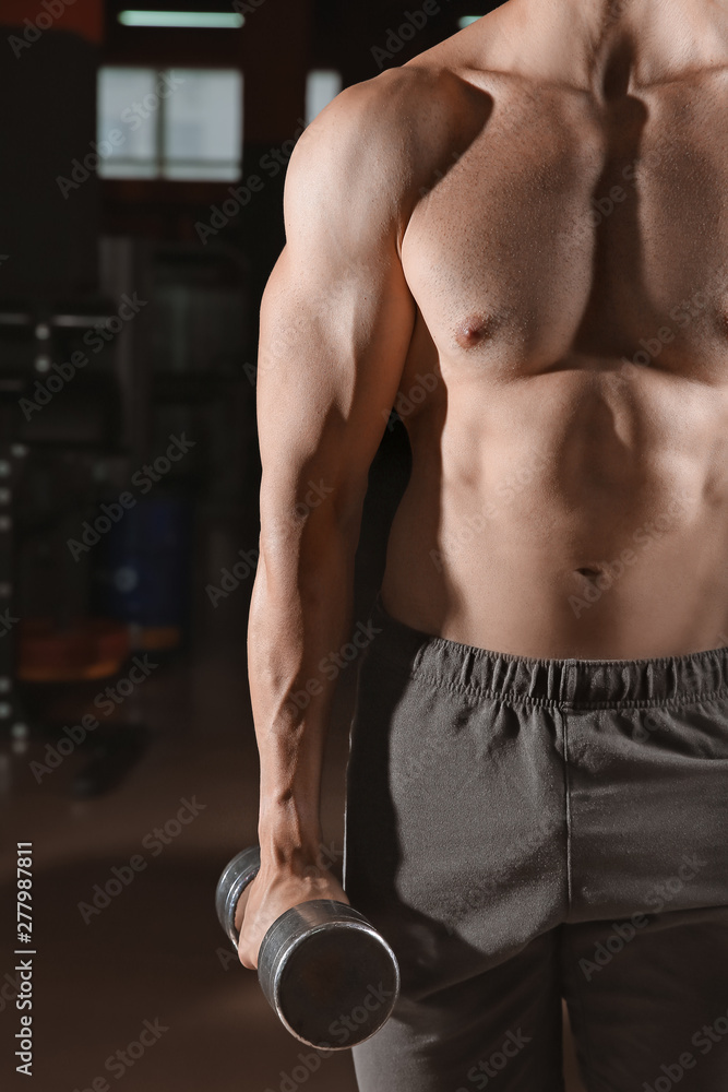 Naklejka premium Sporty young man with dumbbells in gym