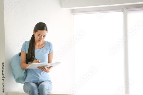 Young Asian student preparing for exam near window