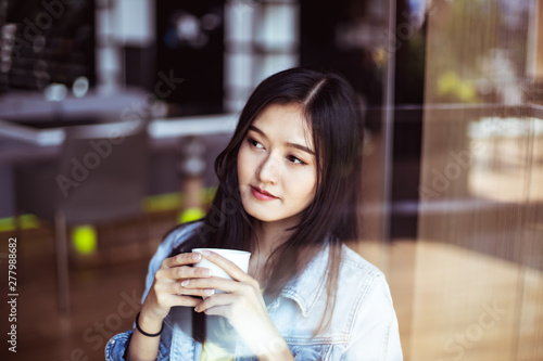 Asian woman with beautiful smile hold mobile phone during rest in coffee shop.Attractive woman drinking coffee.Reflection glass window.
