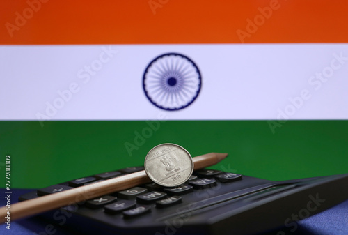 One Rupee coin of India on the calculator and pencil with Indian flag background.
