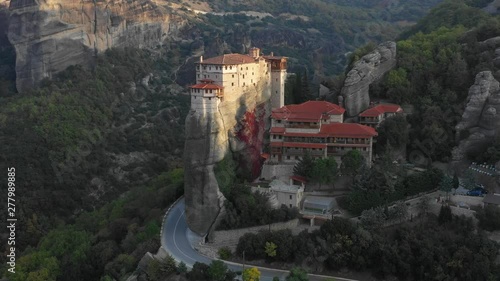 Aerial view of amazing St. Barbara Rusanu Monastery in early sunny morning among mountains and roads in Meteora in Greece. Concept of protected places. 4k DJI Mavic 2 footage video photo