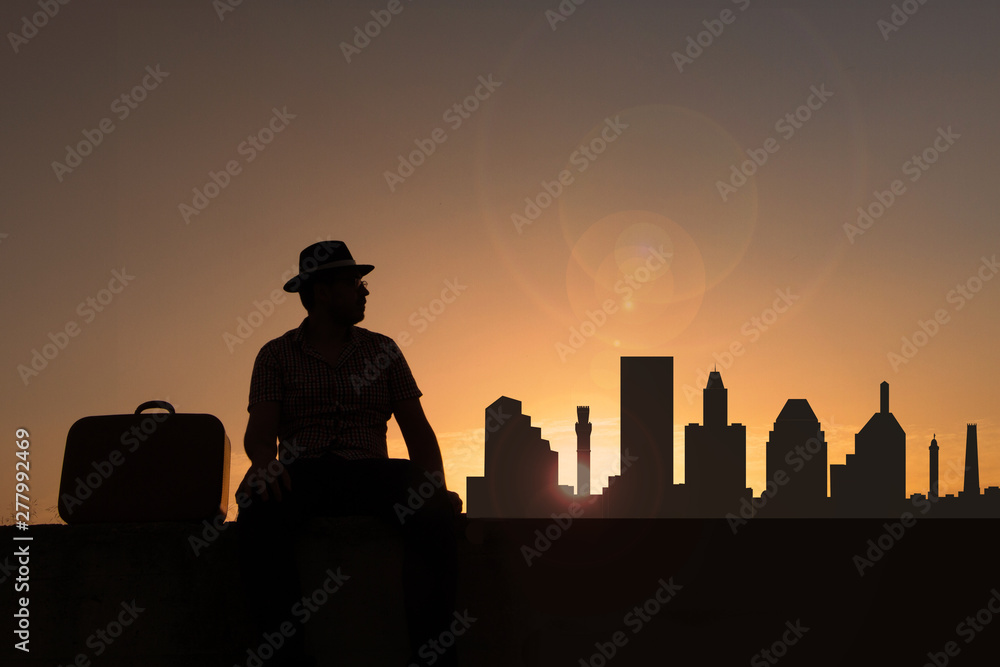 Traveler with suitcase and hat in front of Baltimore city skyline in USA