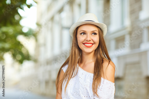 Beautiful girl in white clothes and hat on a city street.