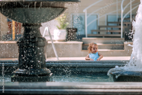 Little beautiful sweet girl walks near the fountain.