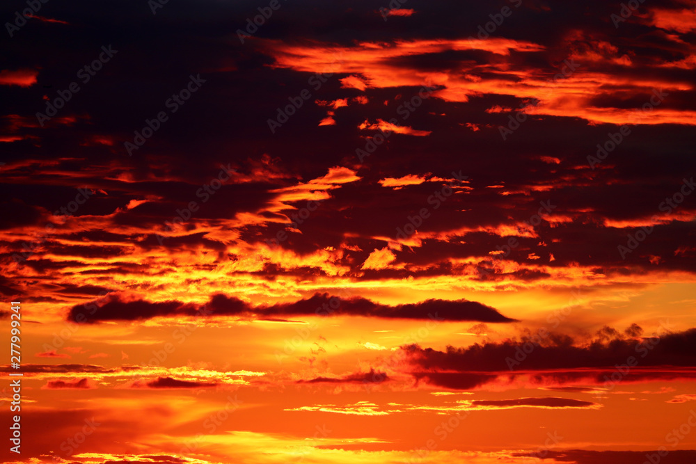 Sunset on colorful dramatic sky, dark clouds in the orange sunlight. Picturesque landscape for horror background