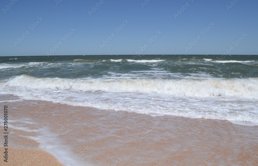 Sea view with foamy waves and sandy beach.