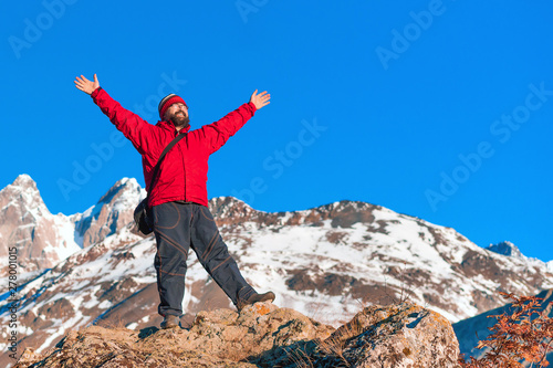 A man in a red jacket with his hands up in the mountains. photo