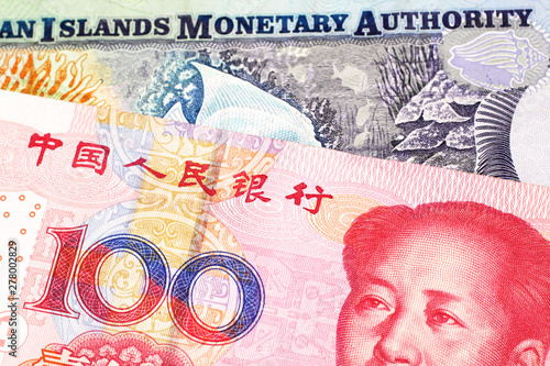 A Chinese, red one hundred yuan renminbi bank note close up in macro with colorful money from the Cayman Islands photo