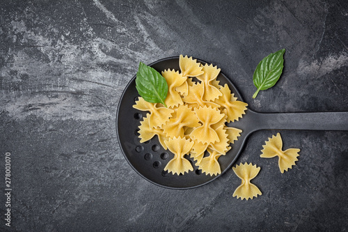 Raw farfalle pasta in black skimmer with basil