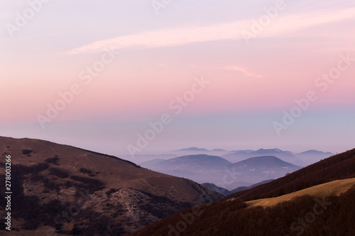 Beautifully colored sky at dusk, with mountains layers and mist between them © Massimo