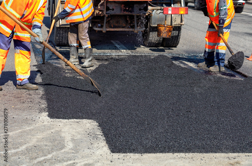 The working team smoothes hot asphalt with shovels by hand when repairing the road.