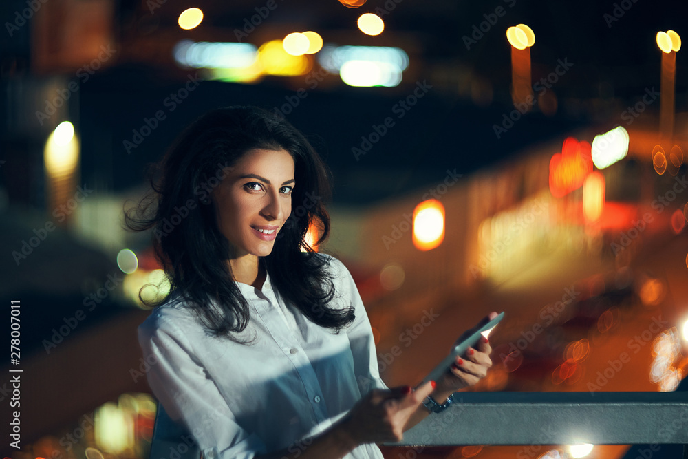 Woman over night cityscape holding a digital tablet texting
