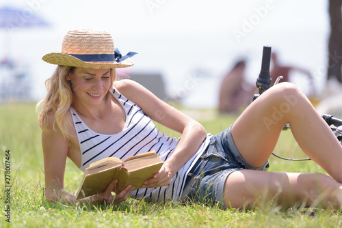 woman reading book on grass with glass and hat