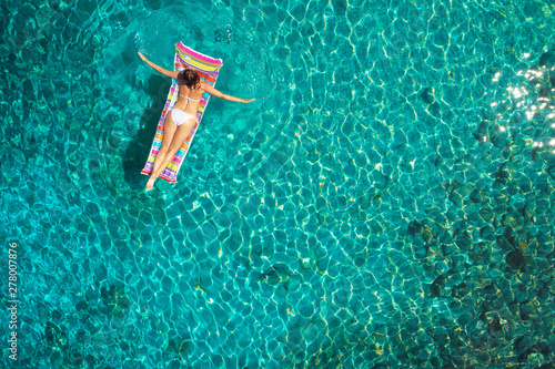 A beautiful young girl lies on a mattress in the open sea or in the pool, a pink bikini, blue clear water, a top view.