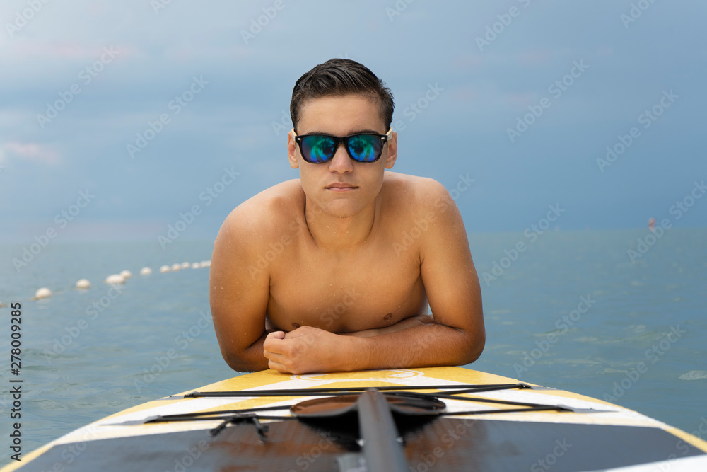 Fashion model in sunglasses posing in the water with sup surfboard. Water sports, fashion and style
