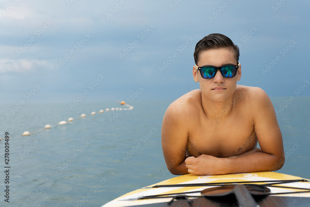 Surfer in sunglasses posing with surfboard on the beach. Active lifestyle and summer vacations. Copy space