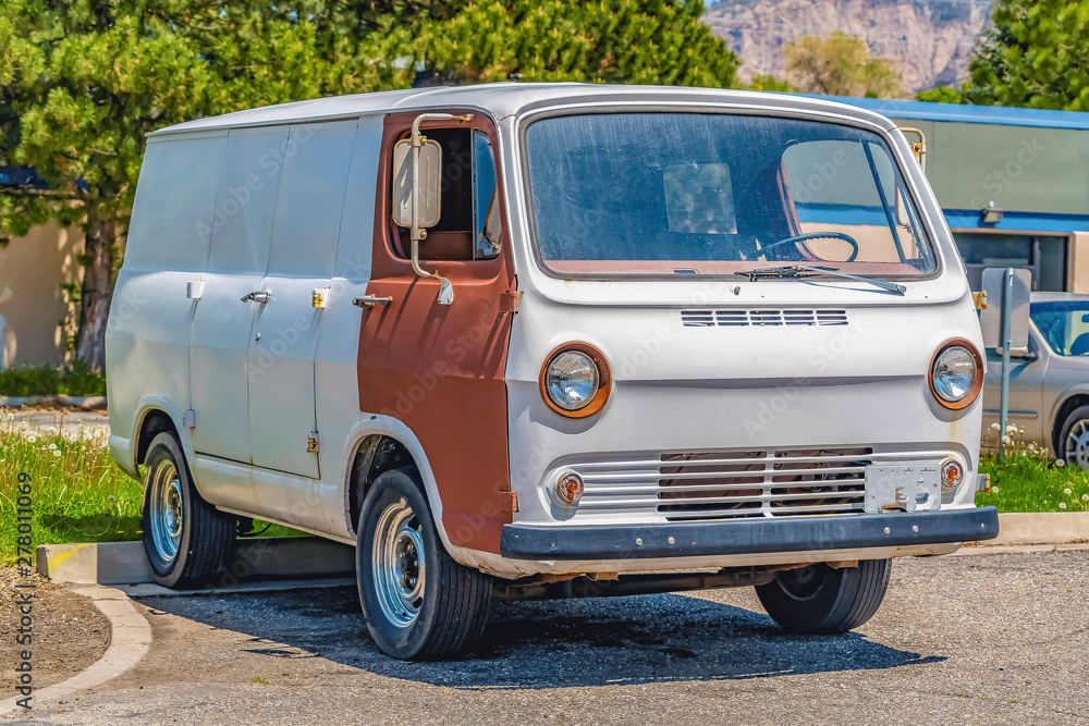 Front view of an old white van with brown door parked on concrete paved ground