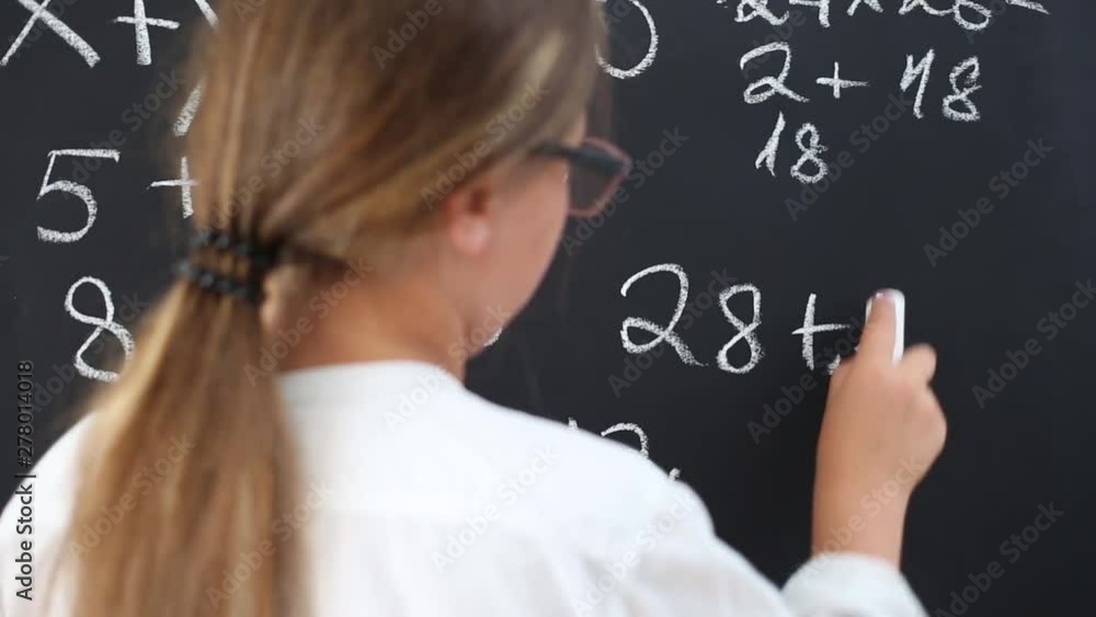 The girl in glasses writes with chalk on the school board in class. The girl in glasses writes with chalk on the school board in class.