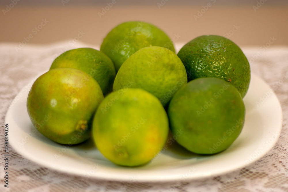 Green lemons served on white porcelain plate on a table covered with white lace towel. Green lemons served on white porcelain plate on a table covered with white lace towel.