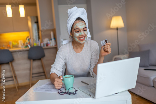 Woman with cosmetic face mask shopping online from her home. Leisure time at home. pPortrait of beautiful woman with facial taking a coffee at home while use internet with modern laptop computer