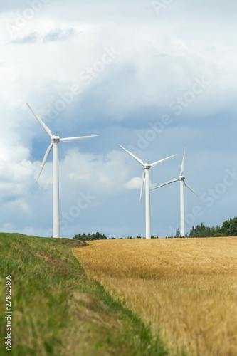 Group of three wind turbines against the sky and a field of ripe wheat. Clean energy source