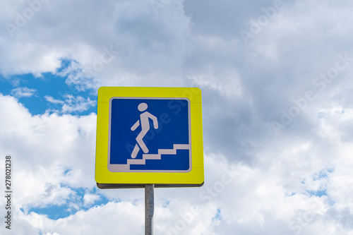 Road sign pedestrian underpass against the blue sky with fluffy clouds. Close-up.