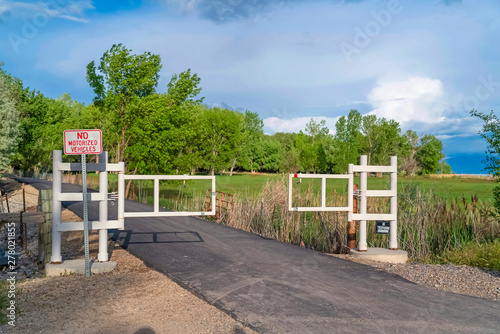 White gate and sign post on a narrow road with grassy field and trees background