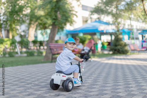 Little cute child riding scooter in city street. Beautiful small toddler boy playing active games outdoors on warm summer or autumn day. Vertical color photo.