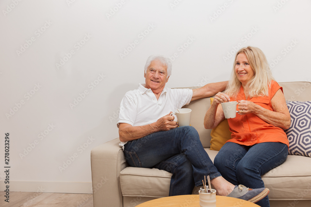 COUPLE SENIOR BUVANT UN CAFÉ SUR UN CANAPÉ COUPLE SENIOR BUVANT UN CAFÉ SUR UN CANAPÉ