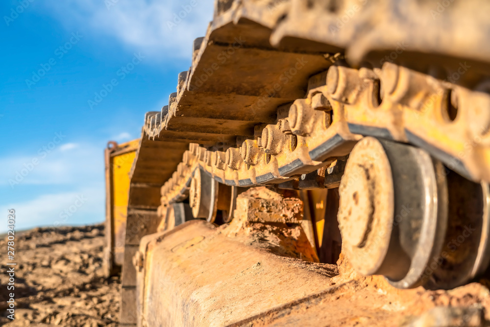 Close up of the dirty track pad and rollers of a yellow excavator on a sunny day