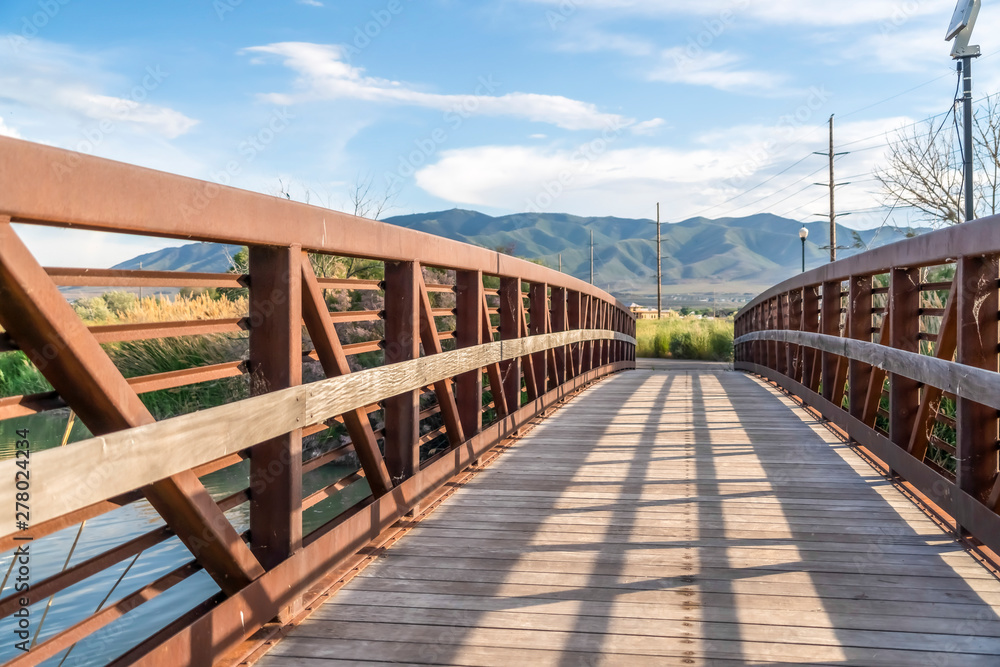 Wooden bridge with metal lattice guardrail over a lake with view of mountain