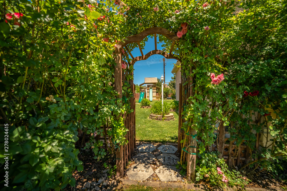 Φωτογραφία Arched wooden arbor at the entrance of a garden with playhouse slides and swings