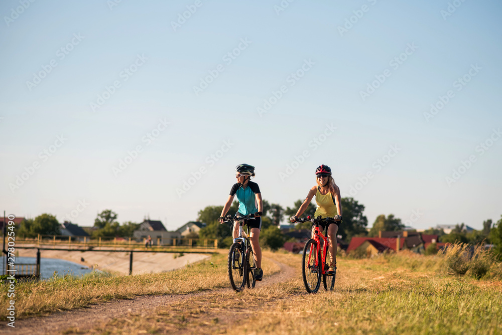 Fototapeta premium Women on bike riding by the lake shore outdoors at the park