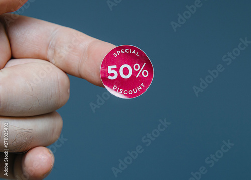 Man hand with glue sticked discount sale special 50 percent off price price red tags to be glued on goods during sale season - isolated gray background