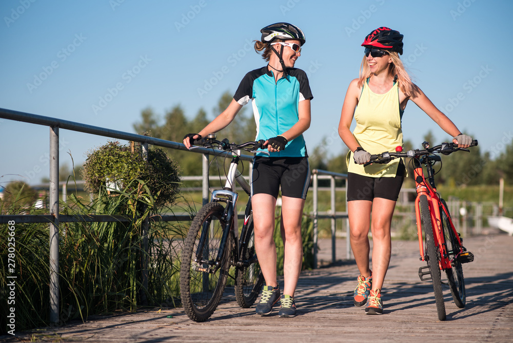 Two female friends walking with bikes and talking each other