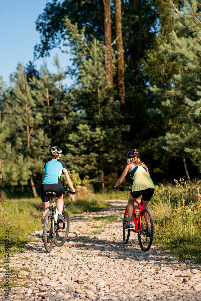 Two women friends riding bikes offroad at the forest