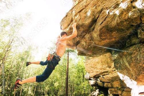 Rock climber climbs bouldering on a cliff on forest. Low angle of strong rock climbing man hanging free on rock with sunflare photo