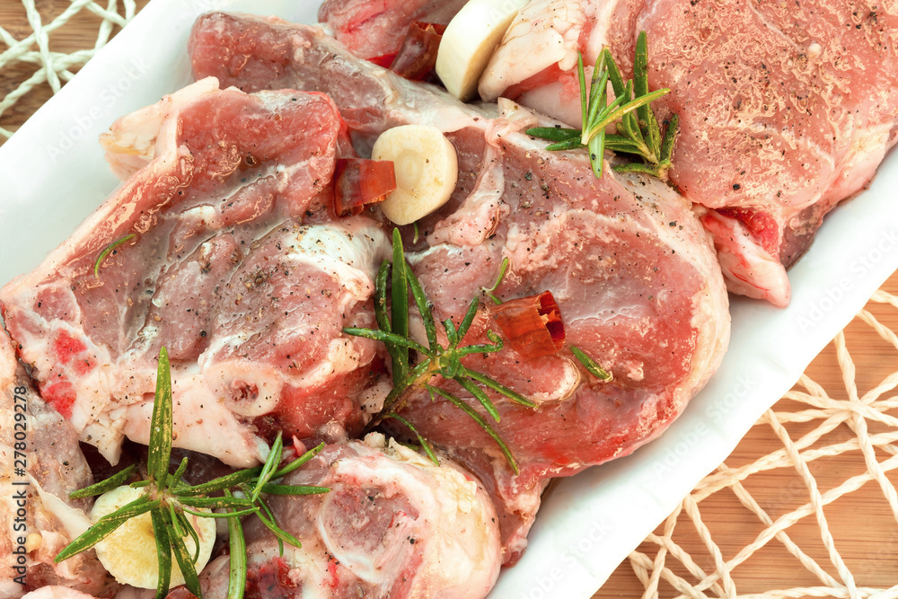 Raw lamb pieces marinated with rosemary, olive oil, garlic and red pepper on a white plate. Close-up. Food photography in high resolution. Flat lay food. Raw lamb pieces marinated with rosemary, olive oil, garlic and red pepper on a white plate. Close-up. Food photography in high resolution. Flat lay food.