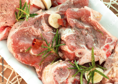 Raw lamb pieces marinated with rosemary, olive oil, garlic and red pepper on a white plate. Close-up. Food photography in high resolution. Flat lay food.